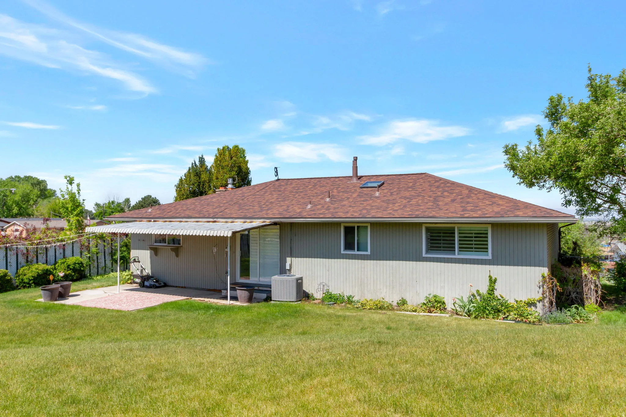 Expansive backyard featuring a manicured lawn, a covered patio area with a concrete surface, and a brown shingle roof