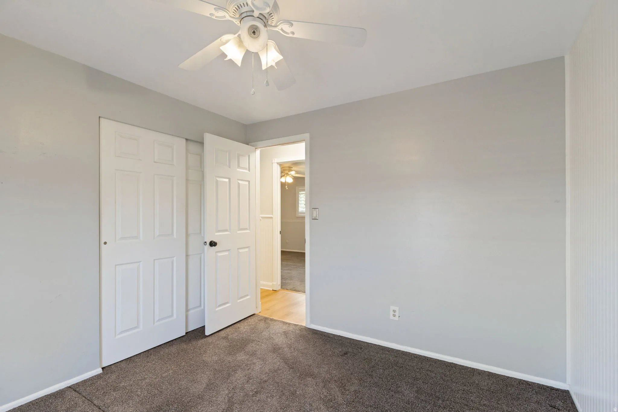 Carpeted bedroom with a ceiling fan light fixture, white six-panel bifold closet doors, and light gray painted walls
