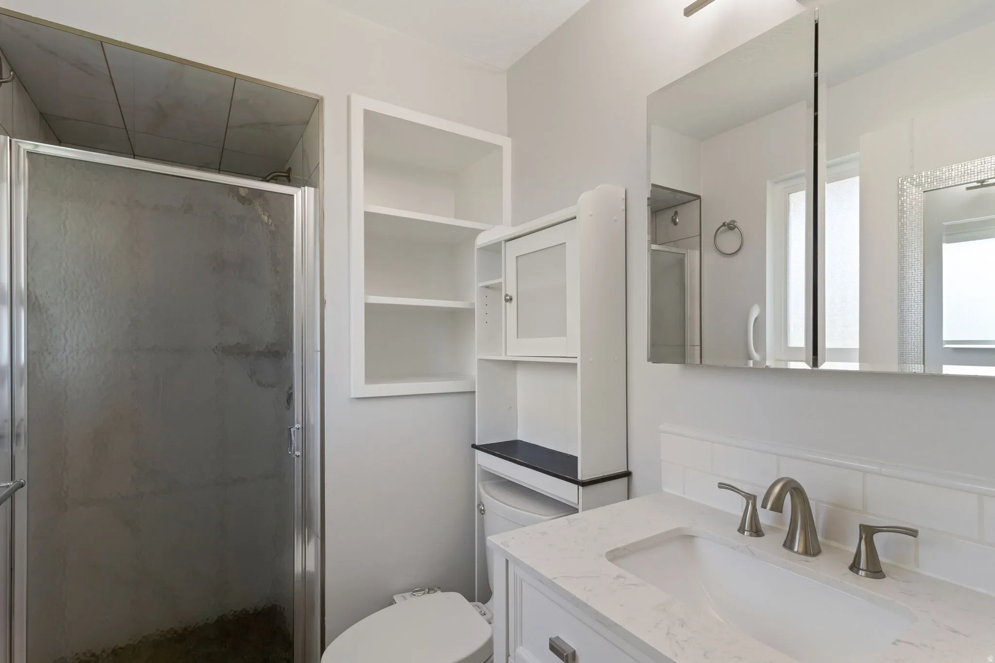Bathroom featuring a glass-enclosed shower with tile surround, a built-in shelving unit, and a vanity with an undermount sink and brushed nickel faucet