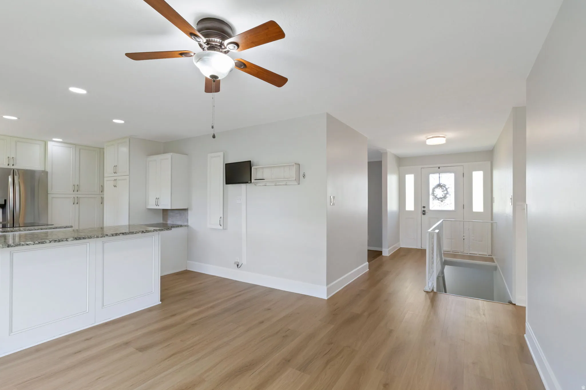 Open-concept living area featuring wood-look flooring, a kitchen with white cabinetry and a breakfast bar, stainless steel appliances, and a ceiling fan with integrated lighting