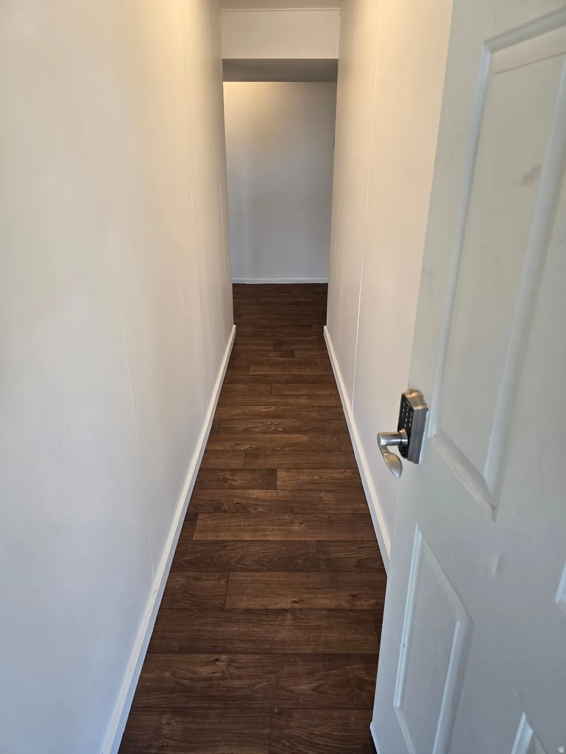 Hallway from the carport with wood-finish flooring, white walls, and white trim