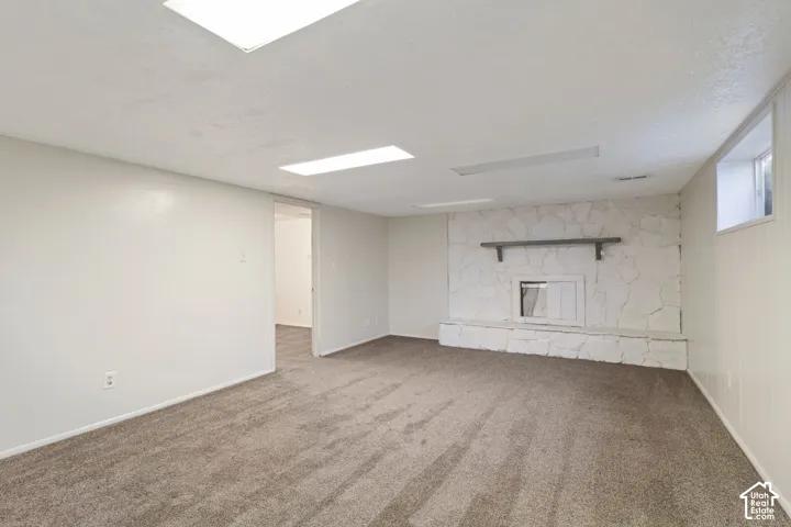 Spacious room featuring a stone-clad fireplace with a mantel, carpeted flooring, white walls, and recessed lighting