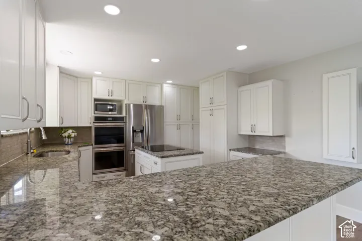Spacious kitchen featuring extensive granite countertops, white cabinetry with brushed nickel hardware, stainless steel appliances including a built-in microwave and double ovens, and a tile backsplash