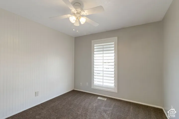 Neutral-toned bedroom featuring a white ceiling fan with integrated lighting, a window with plantation shutters, vertical plank wall paneling, and carpet flooring