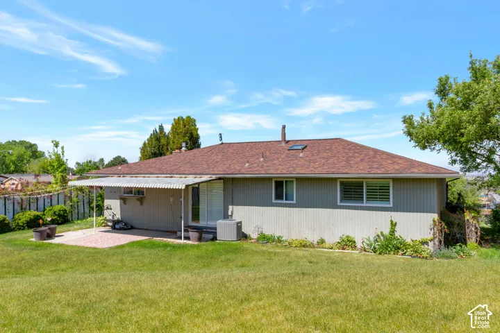 Expansive backyard featuring a manicured lawn, a covered patio area with a concrete surface, and a brown shingle roof