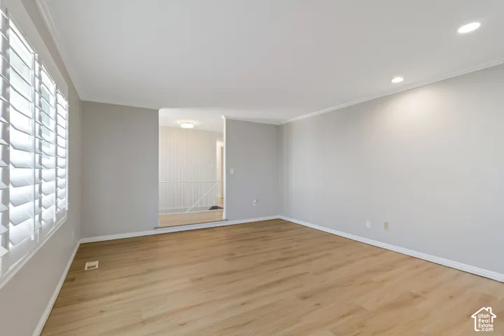 Spacious room featuring light wood-look flooring, plantation shutters, recessed lighting, crown molding, and neutral wall tones