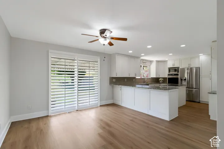 Open-concept living area featuring wood-look flooring, a contemporary ceiling fan, and sliding glass doors with white plantation shutters
