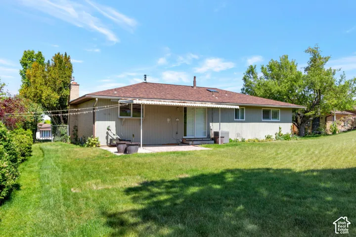 Expansive backyard with a flat lawn, mature perimeter trees, patio area, and a covered awning