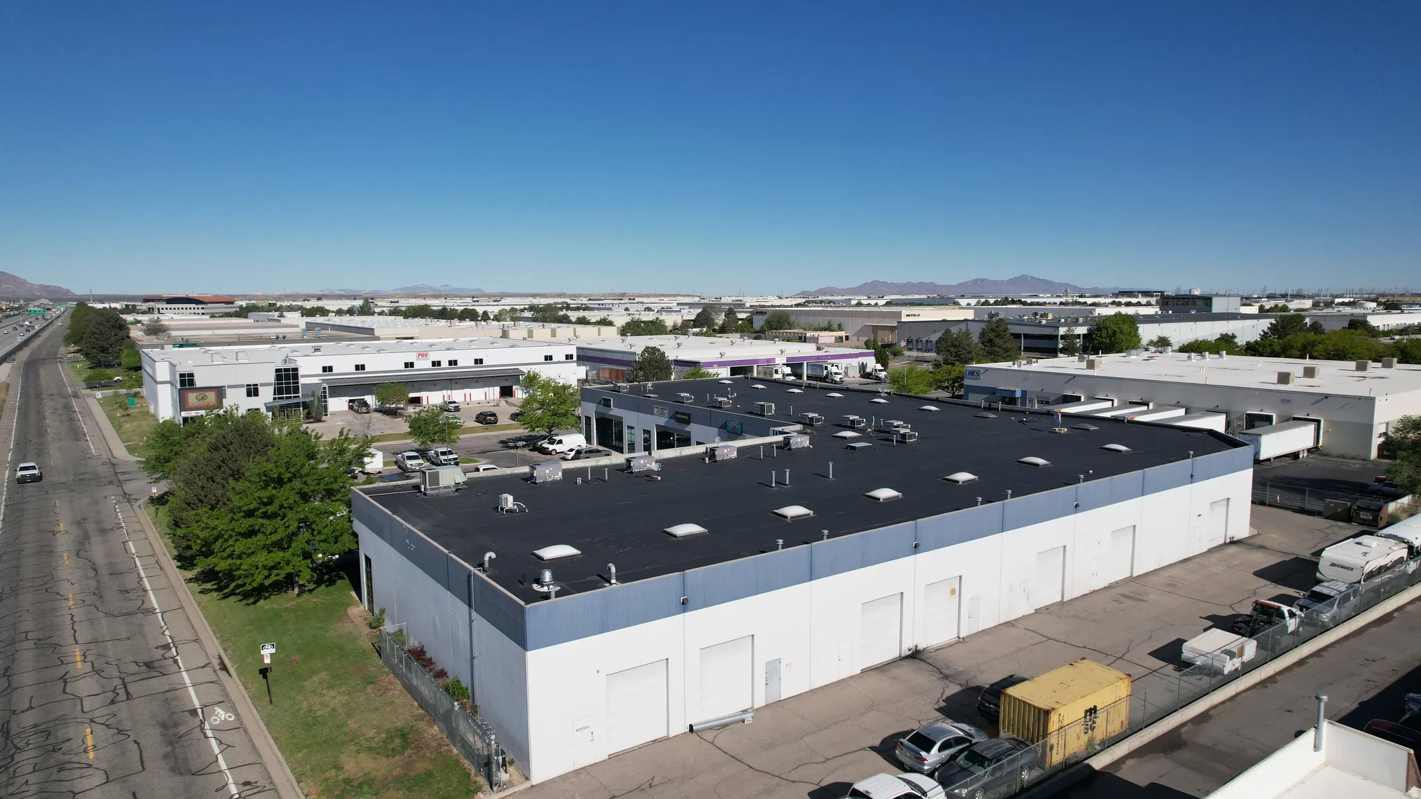 Industrial building featuring multiple garage bay doors, a paved parking area, and a flat roof