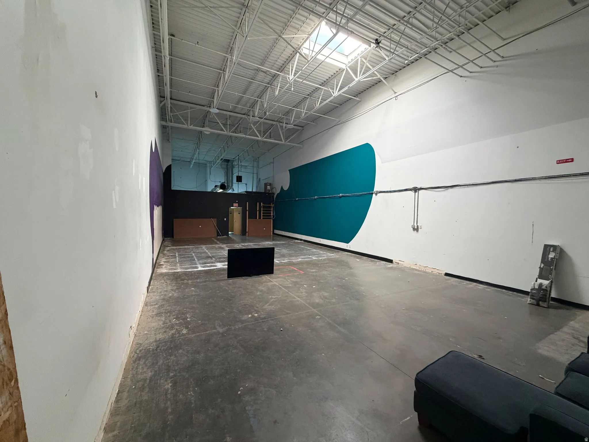 Spacious commercial interior featuring a high exposed ceiling with metal trusses and a skylight