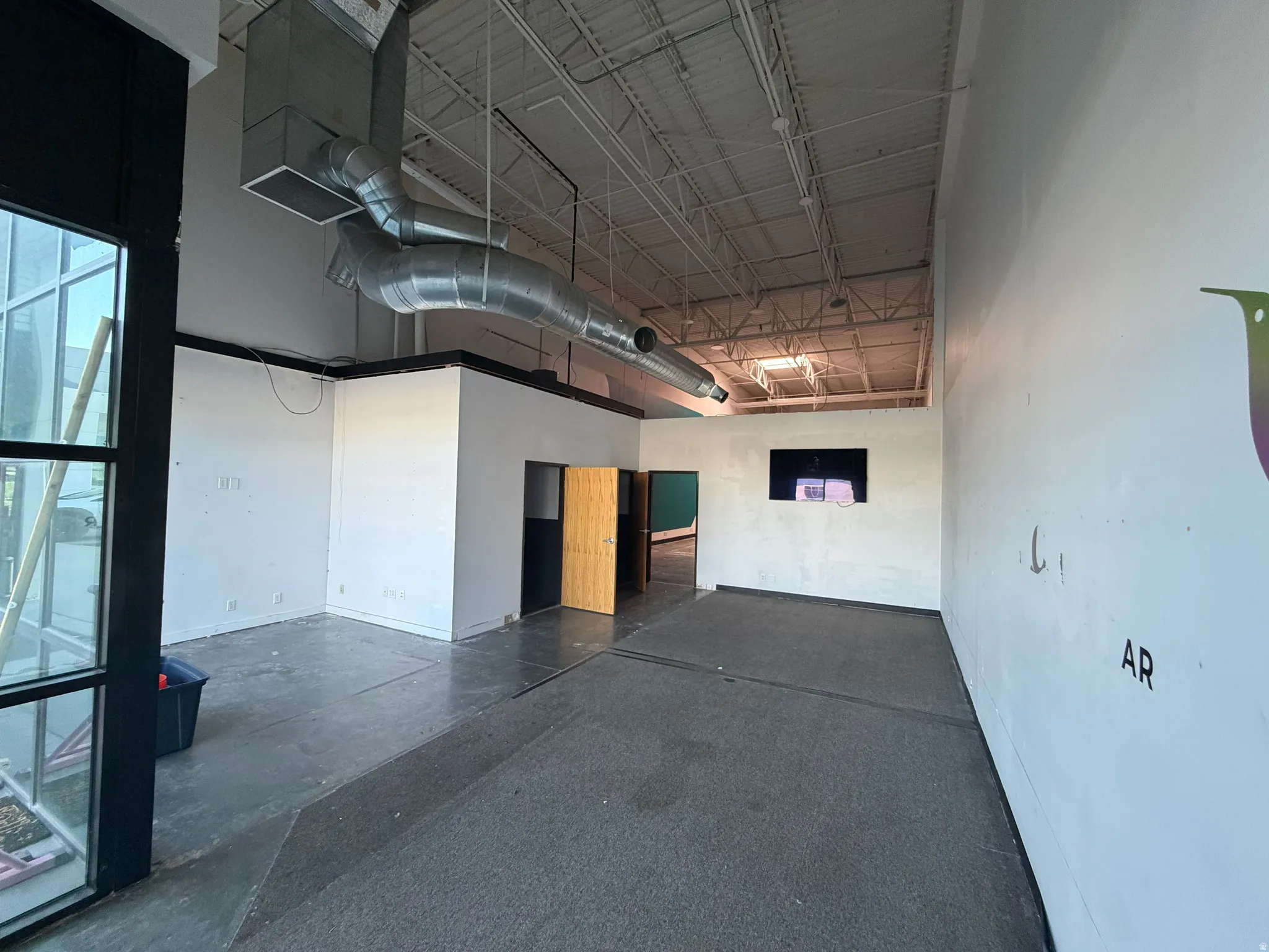 Spacious commercial interior featuring high ceilings, exposed ductwork, and a mix of concrete and carpeted flooring