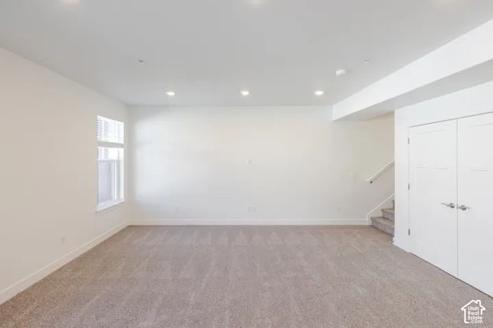Spacious open room featuring neutral wall finishes, recessed ceiling lighting, carpet flooring, and abundant natural light from a side window