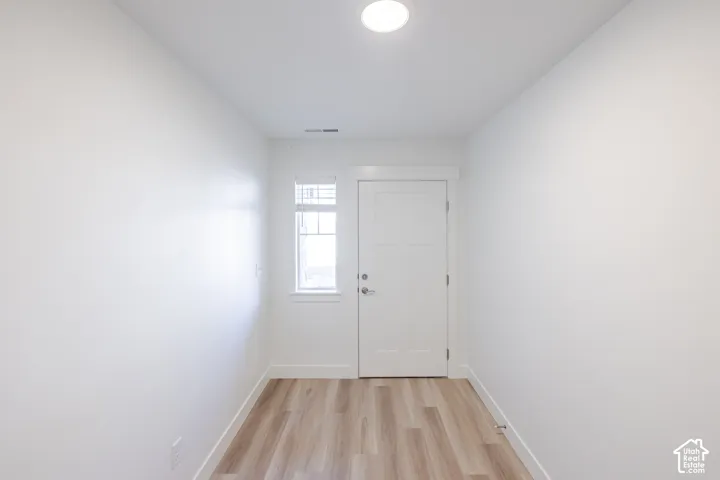 Wood-finish flooring with white trim, a white paneled door, and a single window with white framing
