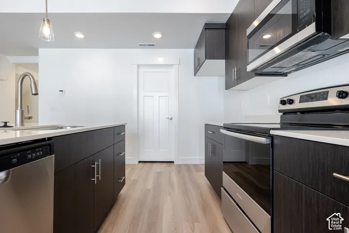 Kitchen featuring dark wood-finish cabinetry, light countertops, stainless steel appliances, and wood-finish flooring