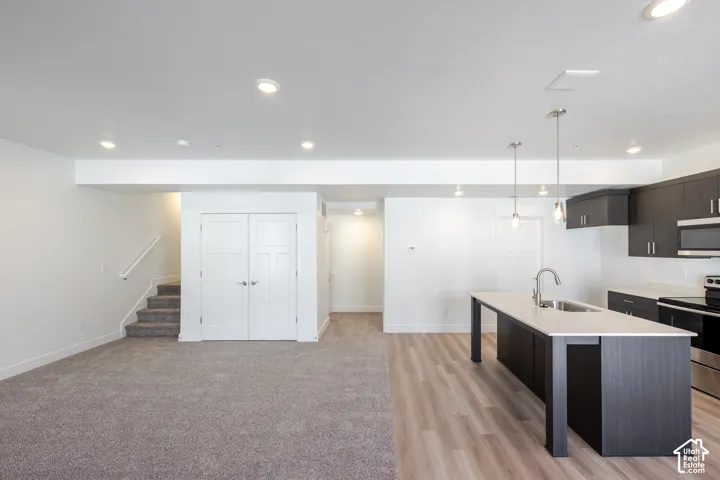 Open-concept lower level featuring a modern kitchen with dark cabinetry, stainless steel appliances, and a large island with seating; wood-finish flooring throughout; recessed and pendant lighting; and a utility closet with double doors