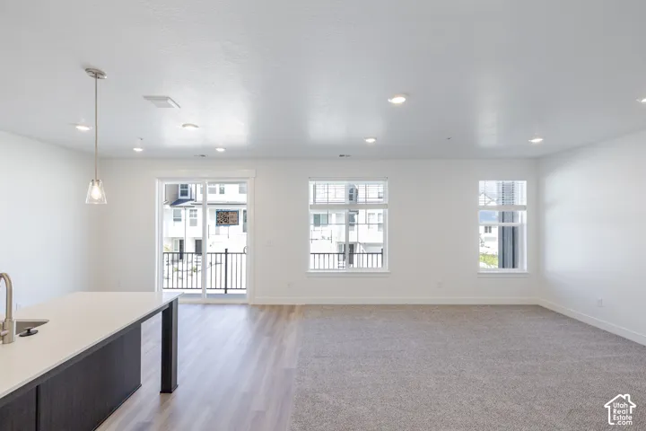 Open concept living area featuring a kitchen island with sink, wood-finish flooring, recessed lighting, and a sliding glass door to a balcony