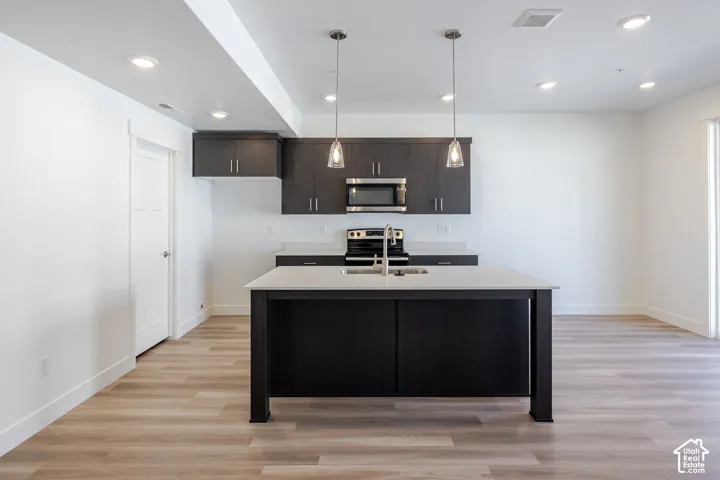 Kitchen featuring dark wood-finish cabinetry, light-toned countertops, and a central island with an integrated sink