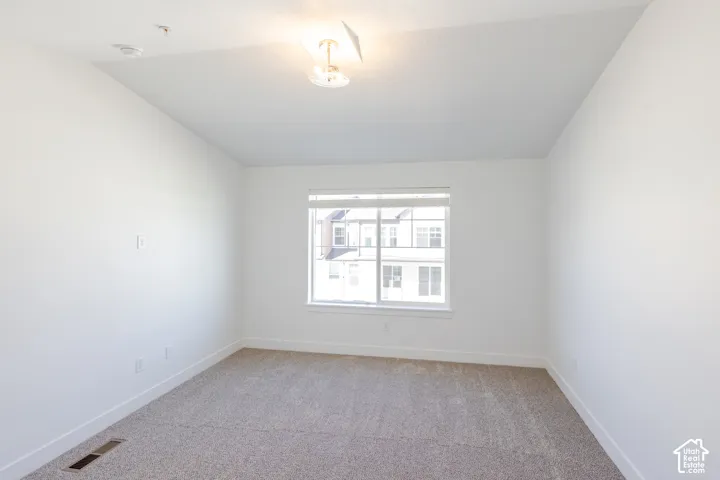 Bright secondary bedroom featuring carpet flooring, a large double-hung window with natural light, white drywall, and a ceiling-mounted light fixture