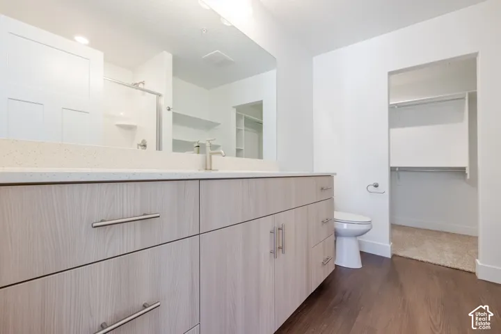Light wood-finish vanity with brushed nickel hardware, light-toned countertop, dark wood-finish flooring, and white walls