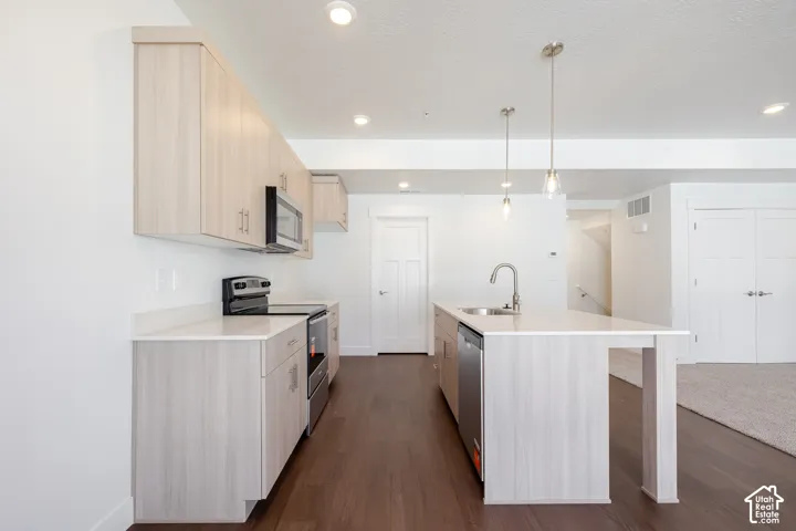 Open-concept kitchen featuring wood-finish cabinetry, stainless steel appliances, a center island with sink, and dark wood-finish flooring