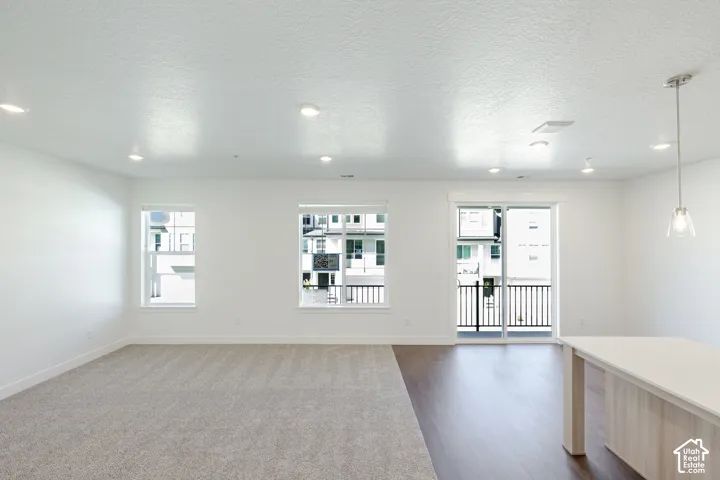 Recessed lighting throughout, carpeted and wood-finish flooring, white walls, multiple windows, and a sliding glass door to a balcony with black railings