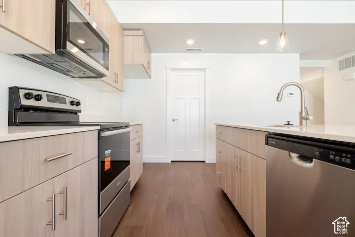 Contemporary kitchen featuring light wood-finish cabinetry, stainless steel appliances, a kitchen island with a sink, and recessed lighting
