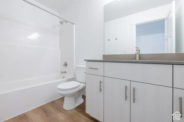 Bathroom featuring a white vanity cabinet with metallic hardware, solid-surface countertop, wood-finish flooring, and a shower-tub combination with a white surround