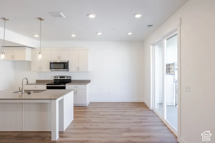 Kitchen featuring white cabinetry, quartz countertops, a central island with a stainless steel undermount sink, pendant lighting, and wood-finish flooring