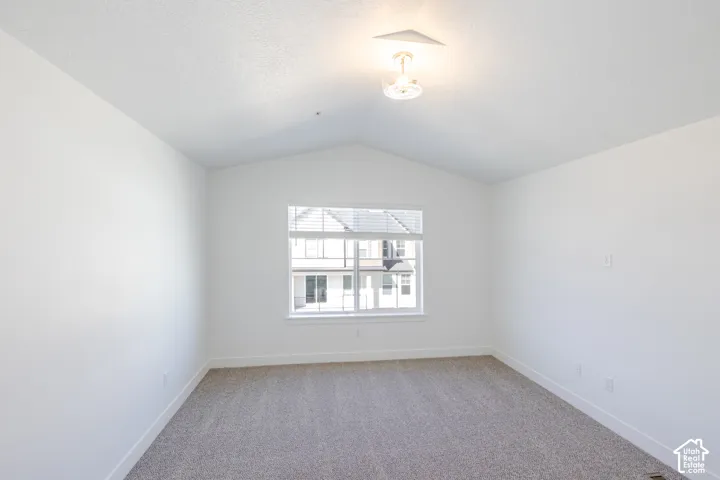 Vaulted ceiling featuring a central flush-mount light fixture, neutral wall finishes, wall-to-wall carpeting, and a multi-pane window with horizontal blinds