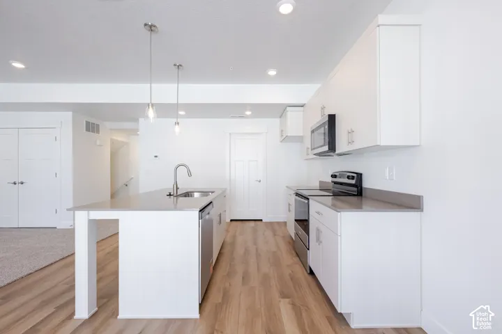 Kitchen featuring white cabinetry, solid-surface countertops, wood-finish flooring, a central island with an integrated sink, and stainless steel appliances