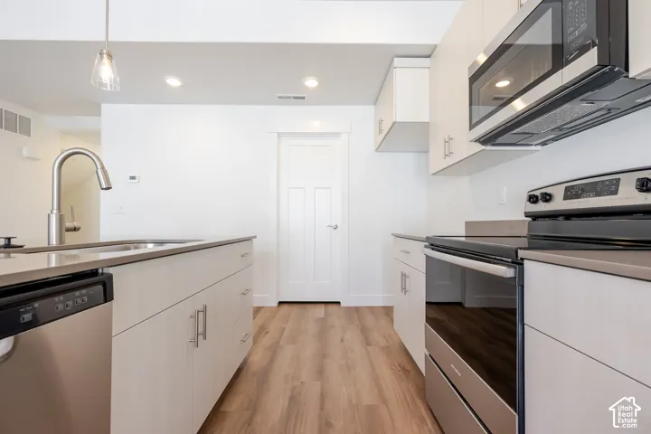 Kitchen featuring light wood-finish cabinetry, stainless steel appliances, quartz countertops, wood-finish flooring, and a gooseneck faucet