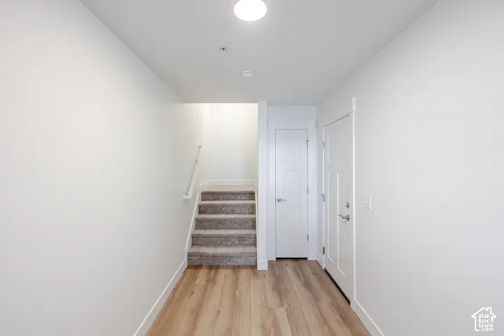 Entryway featuring wood-finish flooring, neutral walls, recessed ceiling lighting, a solid-core interior door, and a carpeted staircase with a wall-mounted handrail