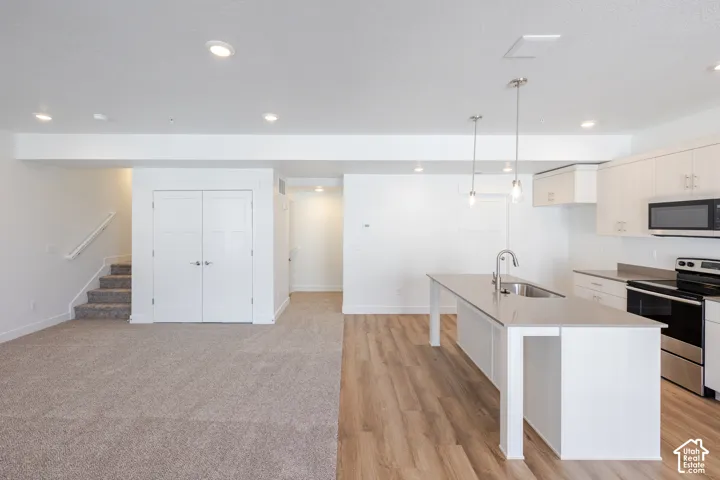 Kitchen featuring white cabinetry, quartz countertops, a central island with a stainless steel sink, wood-finish flooring, and recessed ceiling lighting