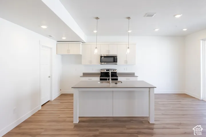 Kitchen featuring white cabinetry, solid-surface countertops, center island with integrated sink, stainless steel built-in microwave, and wood-finish flooring