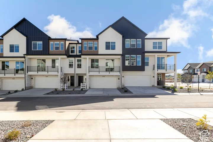 Contemporary multi-level townhome exterior featuring vertical and horizontal siding, metal gable roofing, integrated two-car garages, and second-story balcony railings