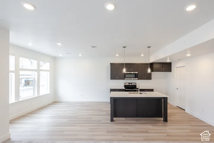 Kitchen featuring a central island with a solid-surface countertop, dark-finish cabinetry, recessed lighting, and wood-finish flooring
