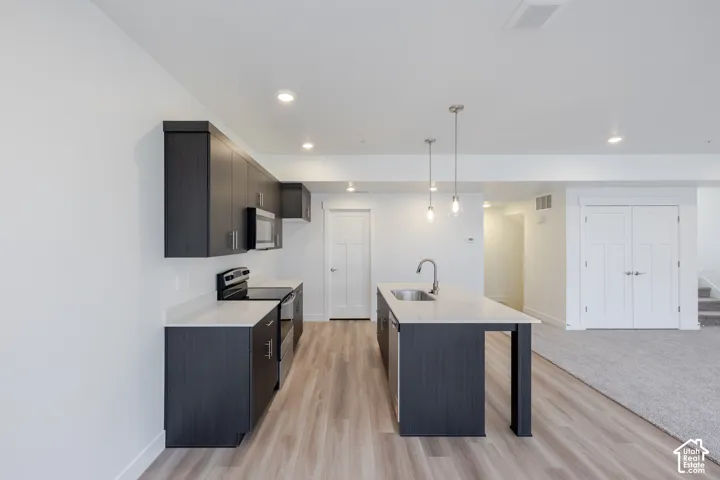 Kitchen featuring dark wood-finish cabinetry, quartz countertops, a central island with an integrated sink, stainless steel appliances, and wood-finish flooring
