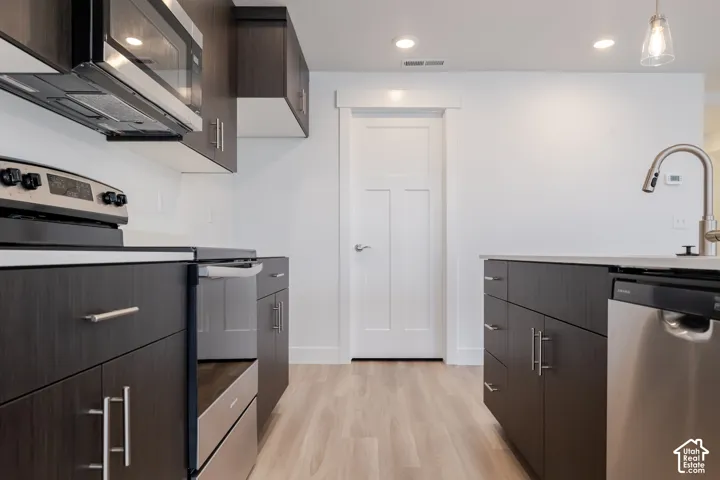Kitchen featuring dark wood-finish cabinetry, stainless steel appliances, a central island with a sink, and light wood-finish flooring