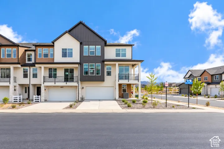 Multi-level exterior featuring a combination of stucco and vertical metal siding, two-car garage with white door, recessed balcony with metal railing, and covered porch