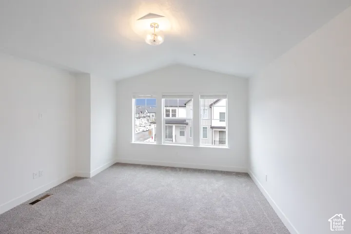 Vaulted ceiling, neutral wall-to-wall carpeting, three-pane window configuration, and glass globe flush-mount lighting fixture