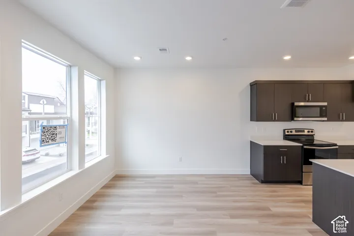 Open-concept interior featuring light-toned wood-finish flooring, recessed lighting, expansive windows, dark-finish cabinetry, and a stainless steel built-in microwave