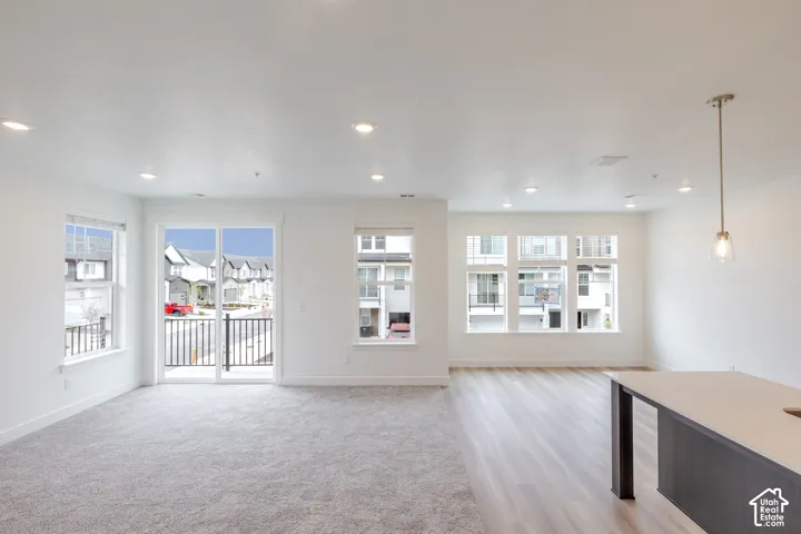 Open-concept interior featuring recessed lighting, large windows with natural light, wood-finish flooring, carpeted floor covering, and sliding glass doors to a balcony