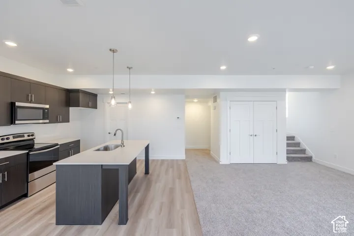 Kitchen featuring dark cabinetry, an island with a light-toned countertop, integrated stainless steel appliances, pendant lighting, and wood-finish flooring