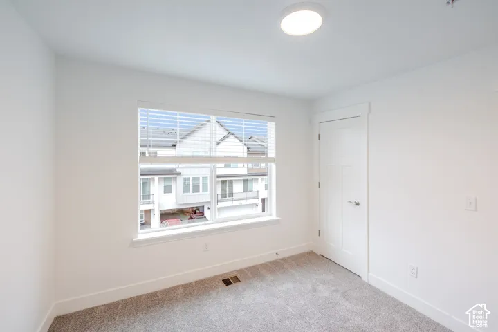 Neutral-toned carpeting, multi-pane window with white trim, solid-panel interior door, and flush-mount ceiling lighting
