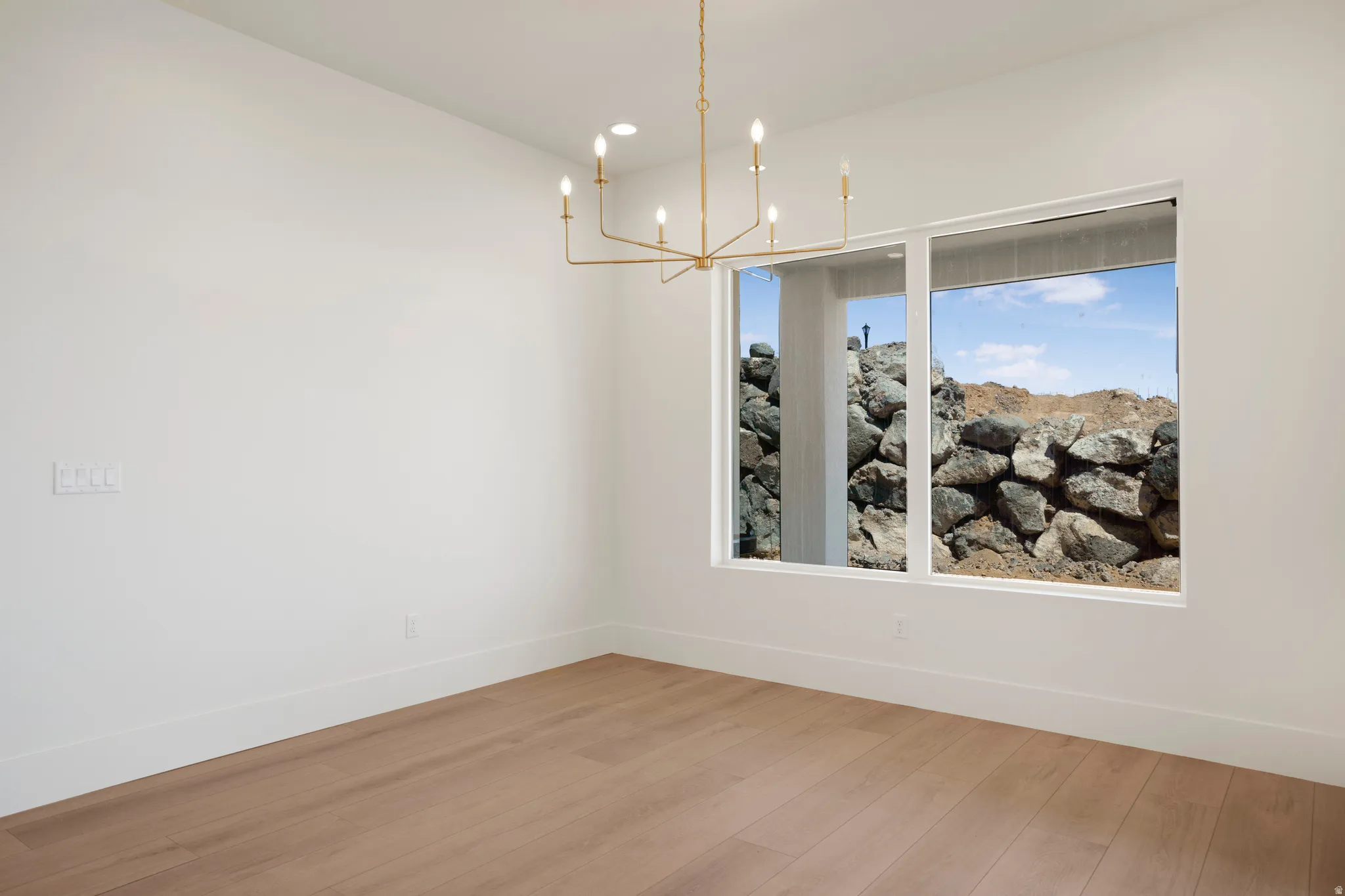 Spacious room featuring wood-finish flooring, crisp white walls, and a contemporary gold-tone chandelier