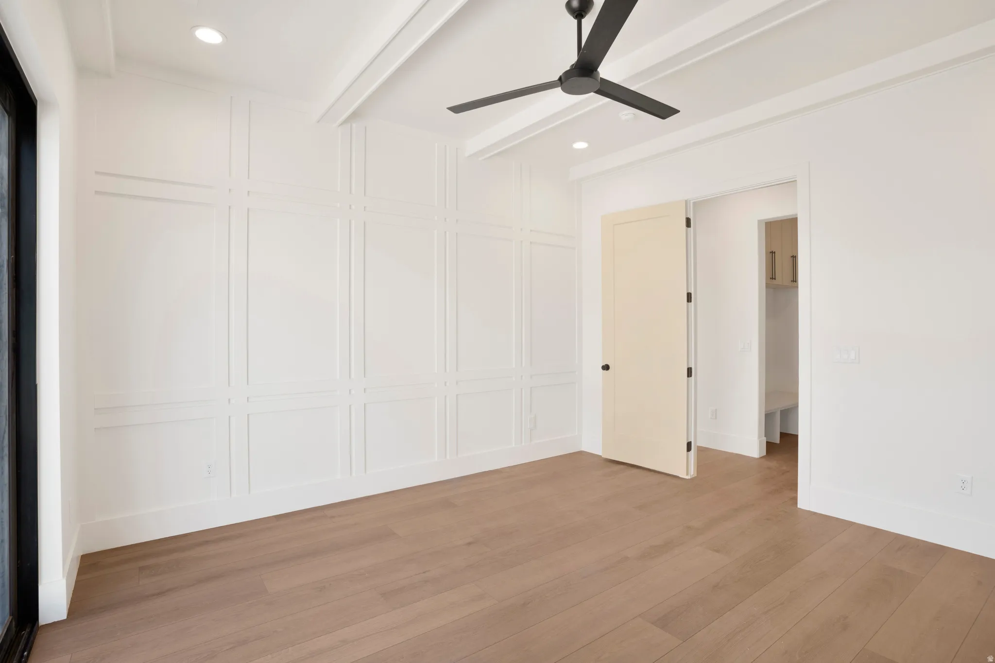 Spacious room with wood-finish flooring, accent wall paneling, and a contemporary ceiling fan