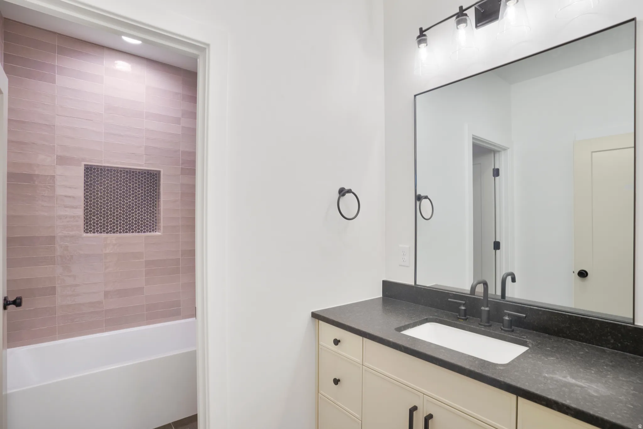 Bathroom featuring a single vanity with a dark countertop, an undermount sink, and black fixtures