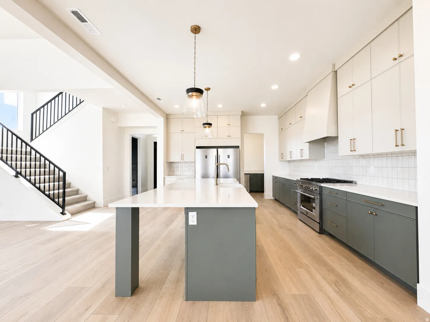 Modern kitchen featuring a large central island with seating, a professional-grade range, stainless steel appliances, and two-tone cabinetry with brass hardware