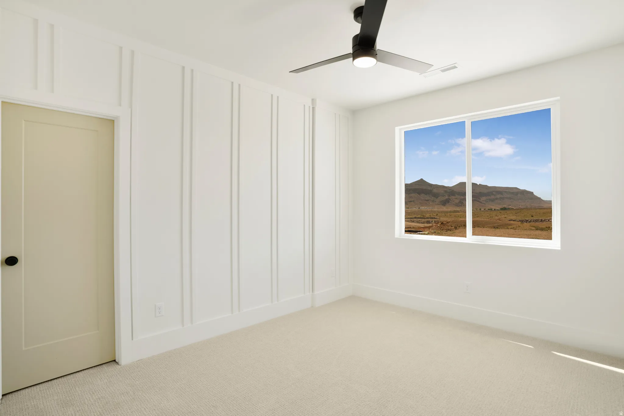 Light-filled interior space featuring a large window, a black ceiling fan with integrated lighting, and a neutral carpeted floor