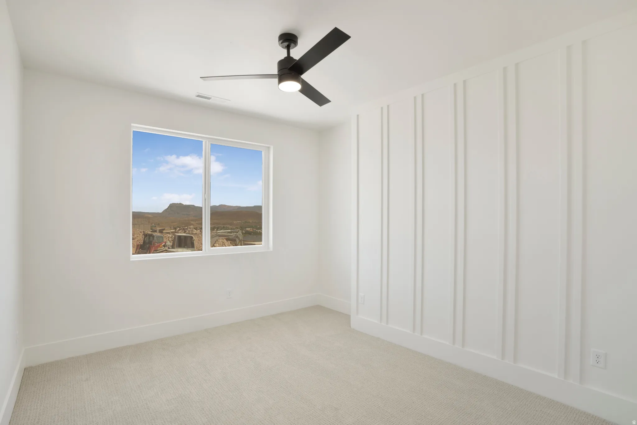 Bright interior space featuring a window with desert scenery, white board and batten accent wall, neutral carpet flooring, and a modern ceiling fan with integrated lighting